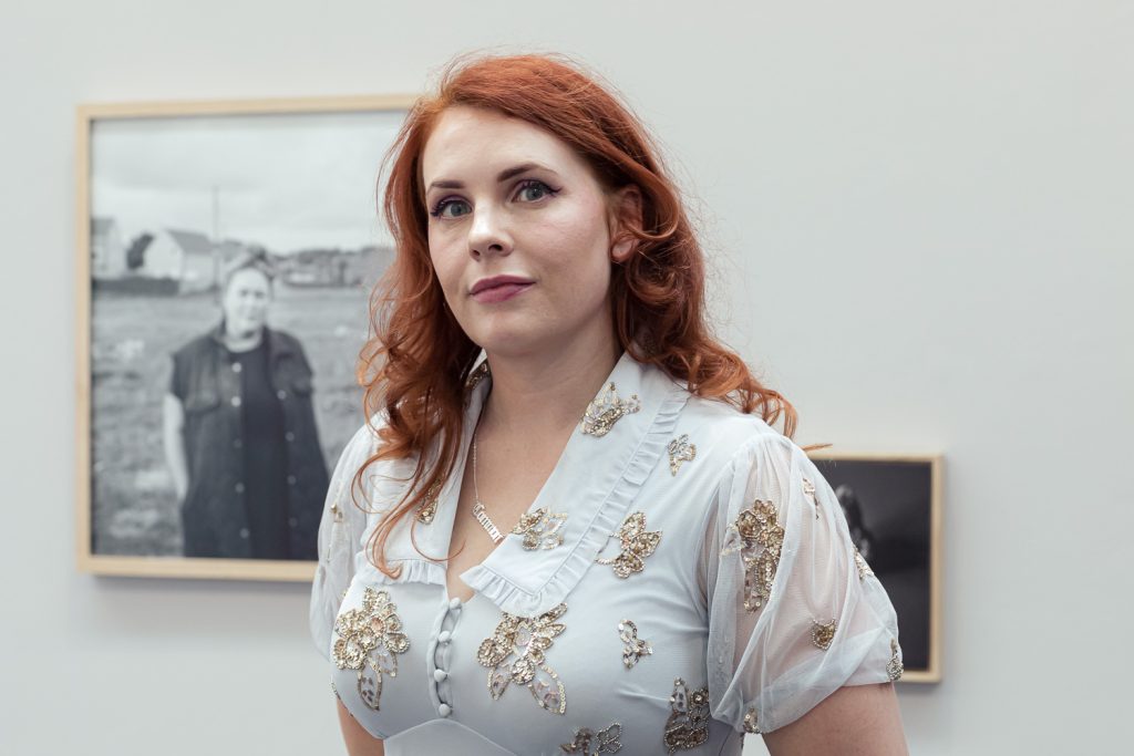 Photo of Joanne with her photography behind her on the wall