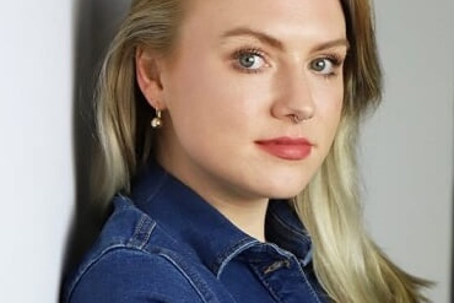 Photo of Emily leaning against a wall, looking over her shoulder at the camera