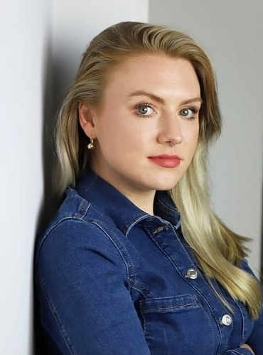 Photo of Emily leaning against a wall, looking over her shoulder at the camera