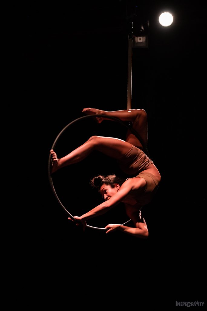 A peron twisted around a hoop suspended in the air.