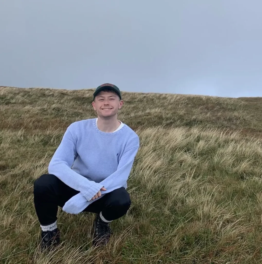 Photo of Dylan crouched in a field smiling at the camera