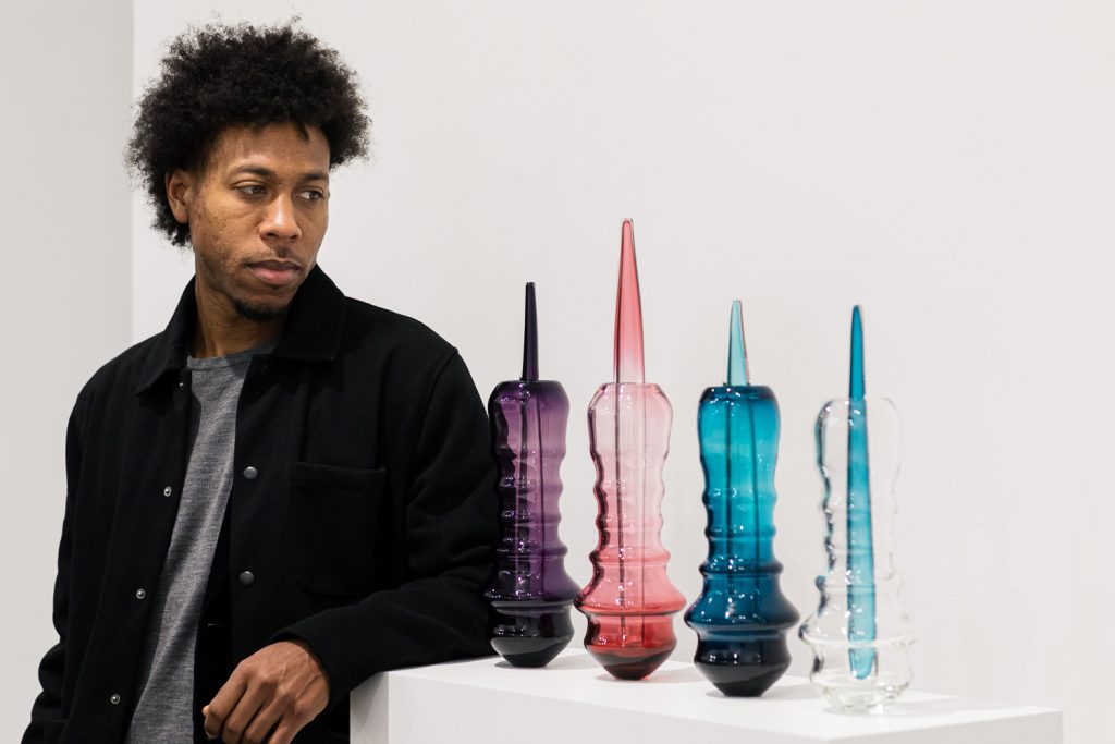 Jahday stood with his elbow resting on a white plinth displaying his glass sculptures