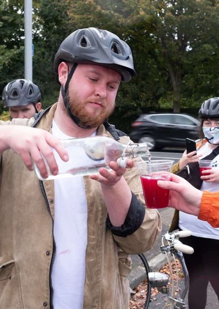 Photo of Phillip wearing a bike helmet and pouring liquid into a cup