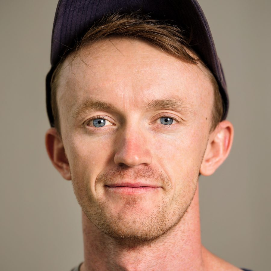 A photo of Fergus from the shoulder up, smiling at the camera. Fergus is wearing a baseball cap.