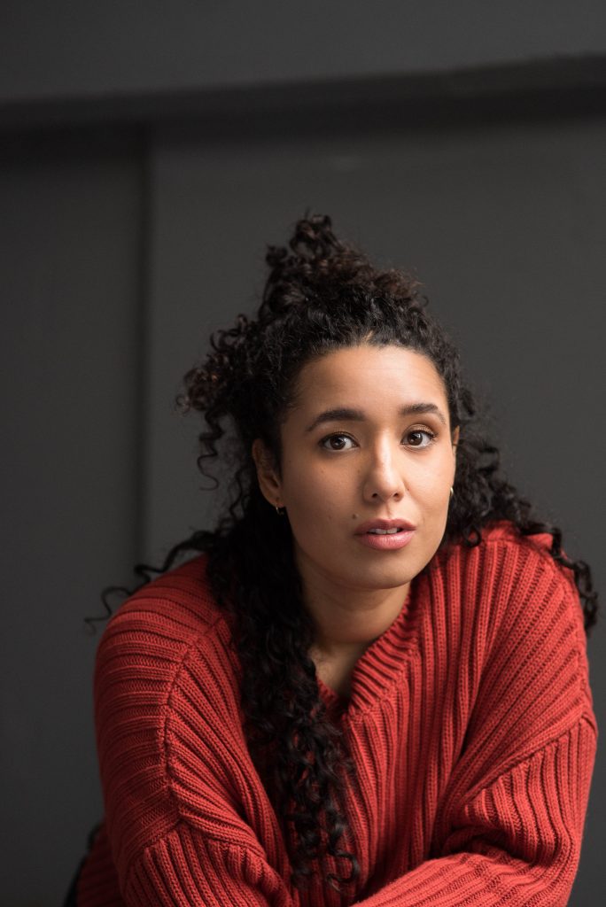 A photo of Josie White looking at the camera. Her hair is tied back and she is wearing a copper coloured cardigan.